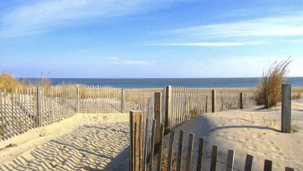 Ein sandiger Strand mit einer Holzumzäunung und blauem Himmel.
