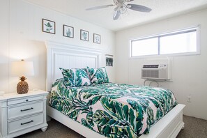 A bedroom with a bed, a nightstand, a lamp, a ceiling fan, and a window with an air conditioning unit.
