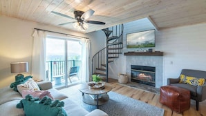 A modern living room with a fireplace, a staircase, and a large window. - Mountain Views Full Kitchen Indoor Pool Access (Gatlinburg)