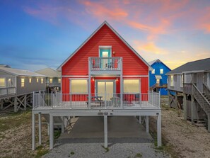 Ein rotes Gebäude mit Balkon, im Hintergrund ein blaues Gebäude und ein hölzerner Deck im Vordergrund.