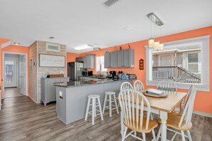 Une cuisine moderne avec des meubles gris, un îlot central et un coin repas avec des chaises blanches.
