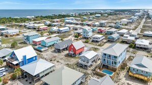 Ett bostadsområde vid kusten med flera hus, varav några har upphöjda konstruktioner, och en fri utsikt över havet.