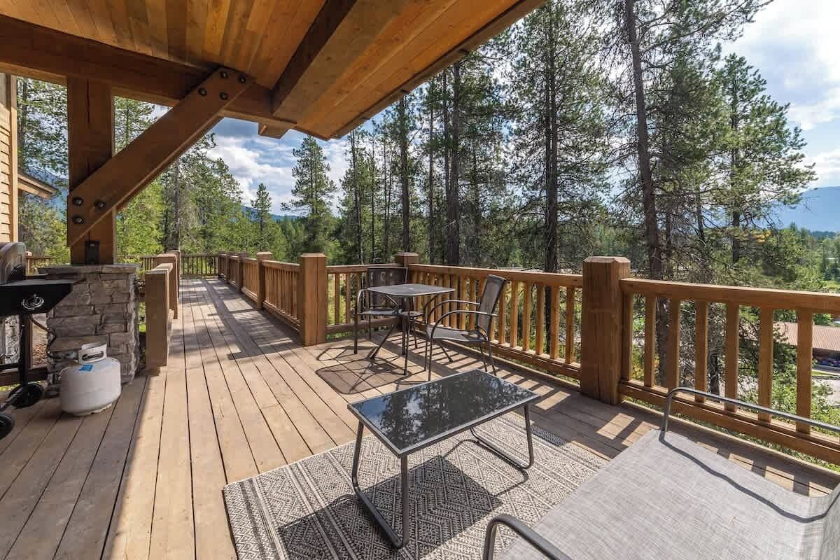 A wooden deck with outdoor furniture, a grill, and a stone wall.