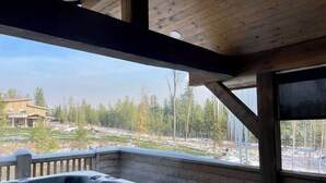 A hot tub in a wooden cabin with a view of a forest and a house in the background. - Luxury Condo•Private Hot Tub•Mtn Views•7 mi to GNP (Coram)