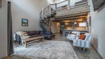A spacious living area with a large rug, a sofa, a bench, and a staircase leading to an upper level.