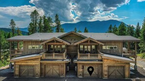 A large wooden cabin with multiple decks and a garage, surrounded by trees and mountains. - Luxury Condo•Private Hot Tub•Mtn Views•7 mi to GNP (Coram)