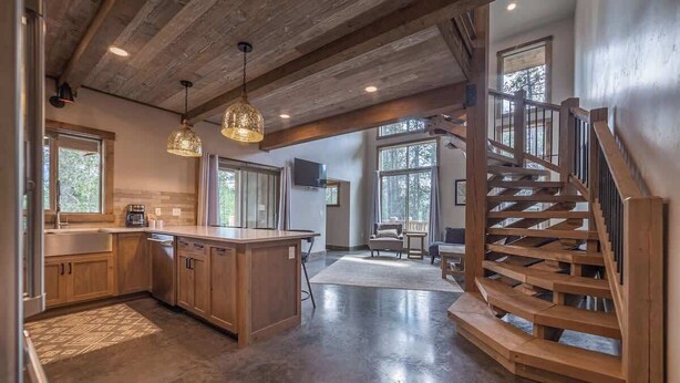 A spacious kitchen with wooden cabinets, a central island, pendant lighting, and a spiral staircase leading to a balcony.