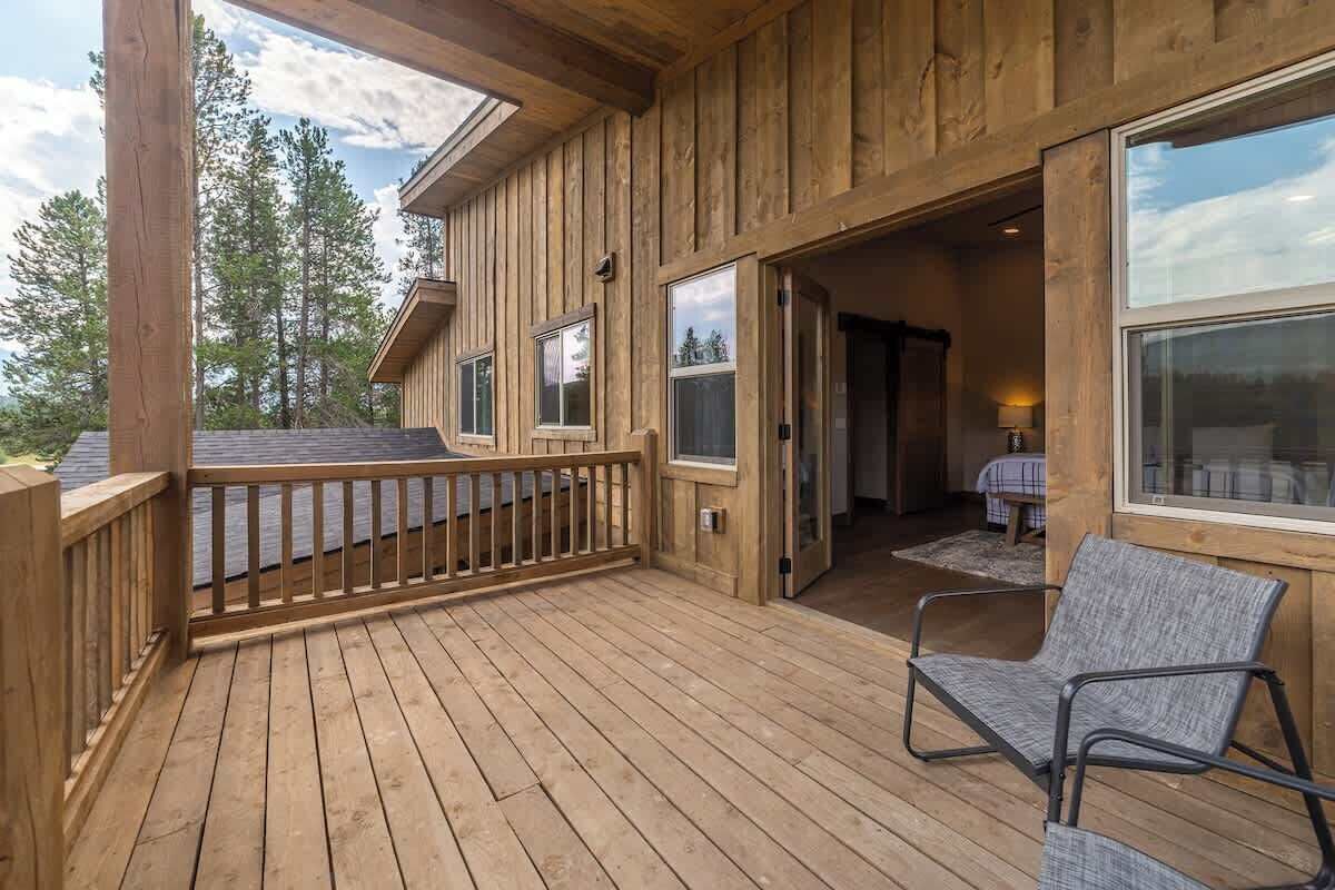 A wooden deck with a chair, a door leading inside, and a view of trees.