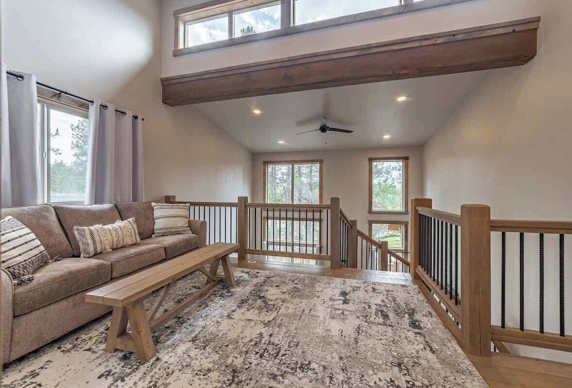 A spacious loft with a high ceiling, a wooden bench, a sofa with cushions, and a view of the outdoors through large windows.