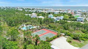 An aerial view of a residential area with houses, a tennis court, and a swimming pool.