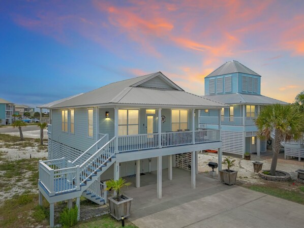 A coastal house with a covered porch, a staircase, and a small tower.