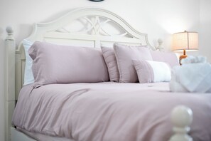 Un lit avec une tête de lit blanche, plusieurs oreillers et une lampe de chevet.