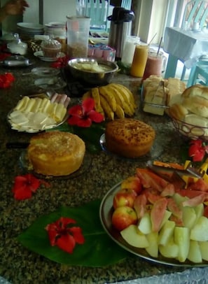 Buffet de café da manhã com diversas frutas, pastelaria e bebidas.