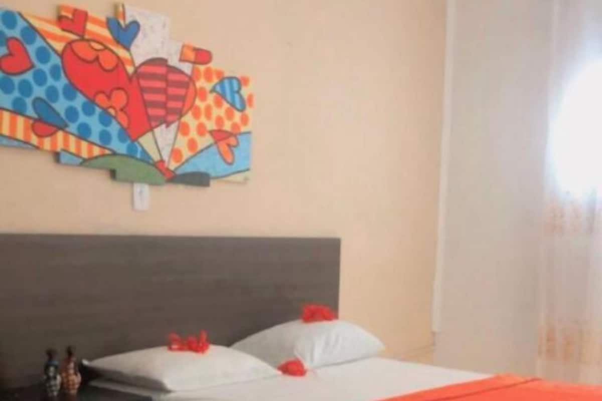 A bedroom with a bed, a nightstand, a dresser, and a colorful abstract painting on the wall.