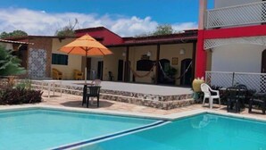 Una piscina con zona de patio, mobiliario exterior y un edificio de techo rojo.