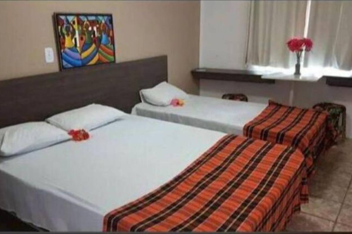 A hotel room with two beds, a painting on the wall, a window with curtains, and a vase with flowers.