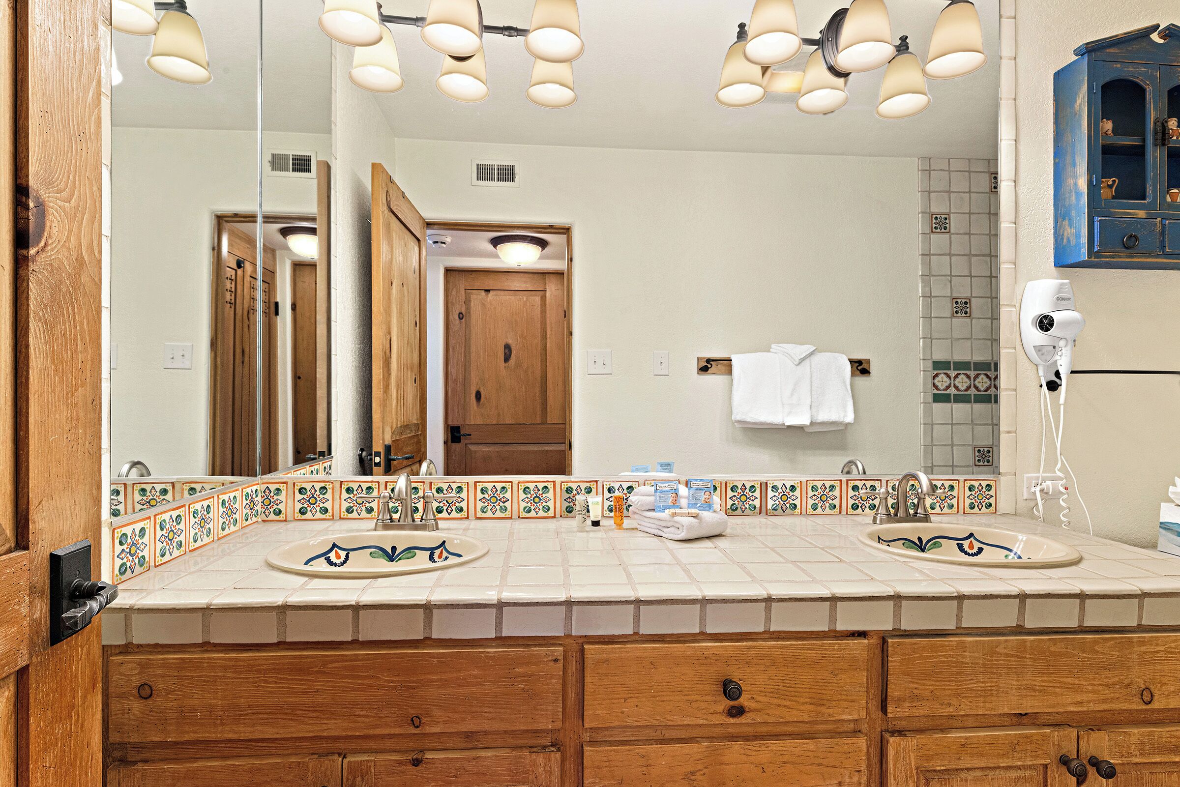 A bathroom with two sinks, wooden cabinets, a large mirror, and a hairdryer.