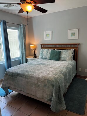 Une chambre à coucher avec un lit, un ventilateur de plafond, une table de chevet avec une lampe et deux tableaux encadrés accrochés au mur.