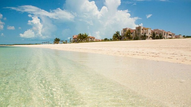 A beach with clear water, a sandy shore, and a row of buildings in the background. - Beautiful 2 bed/2 bath Ocean view  - TripAdvisor winner 2016,2017,2018 and 2019! (Wheeland Settlement)