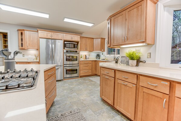 A modern kitchen with wooden cabinets, stainless steel appliances, and a large window.