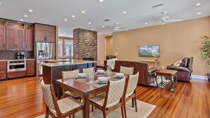 A spacious kitchen with modern appliances, a dining area with wooden furniture, and a living room with a comfortable sofa and a television. - Hyde Park Villa w/ Saltwater Pool + Fire Place! (Sarasota)