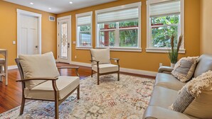 A spacious living room with hardwood floors, a large window with a view of greenery, and a beige sofa. - Hyde Park Villa w/ Saltwater Pool + Fire Place! (Sarasota)