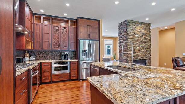A modern kitchen with wooden cabinets, stainless steel appliances, granite countertops, and a stone accent wall. - Hyde Park Villa w/ Saltwater Pool + Fire Place! (Sarasota)