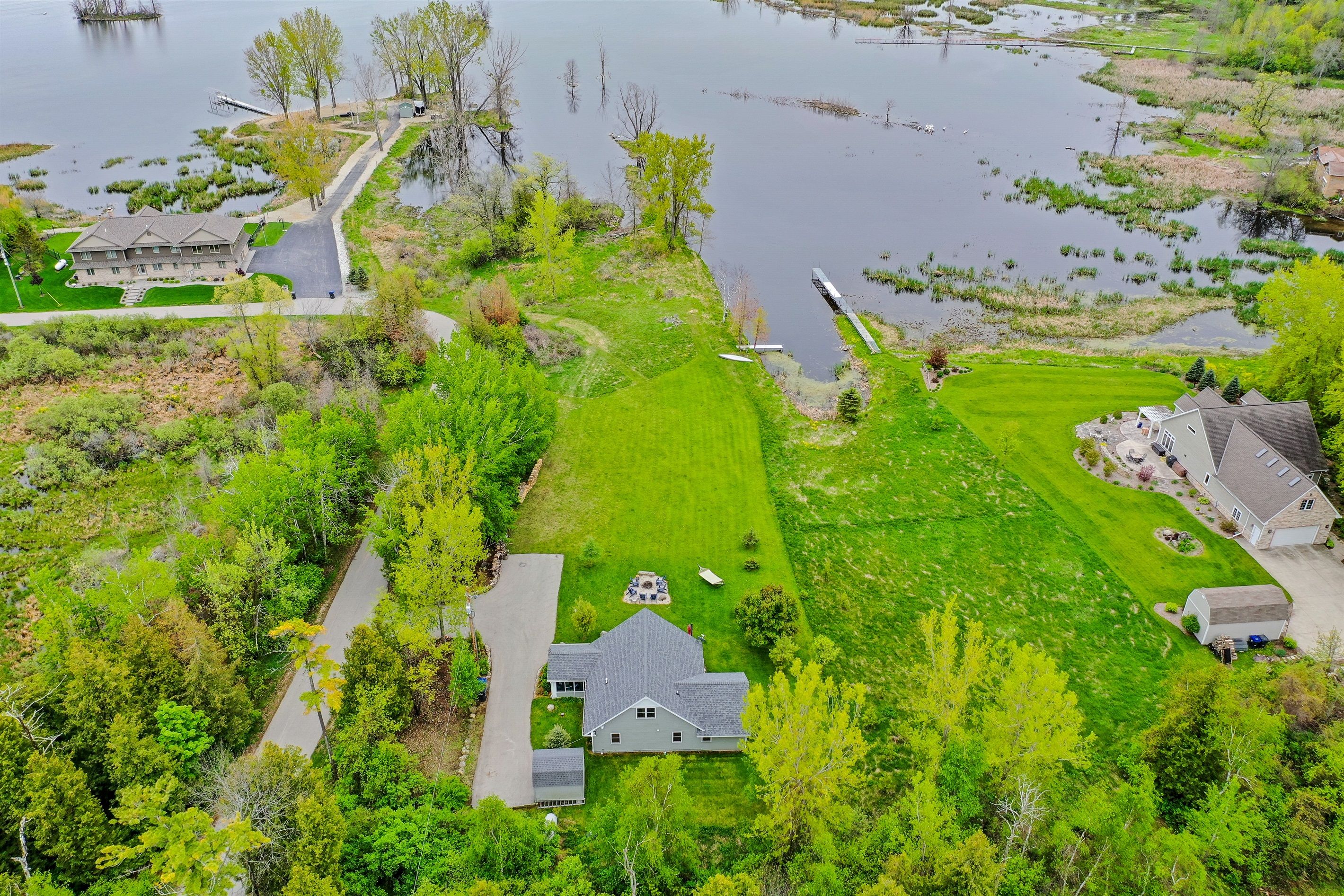 An aerial view of a residential area with a large house, a pond, and surrounding greenery.