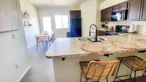 A modern kitchen with a central island, bar stools, and a dining area with a table and chairs. - Yuma Boho/Airy 3 bedroom home with free parking (Yuma)