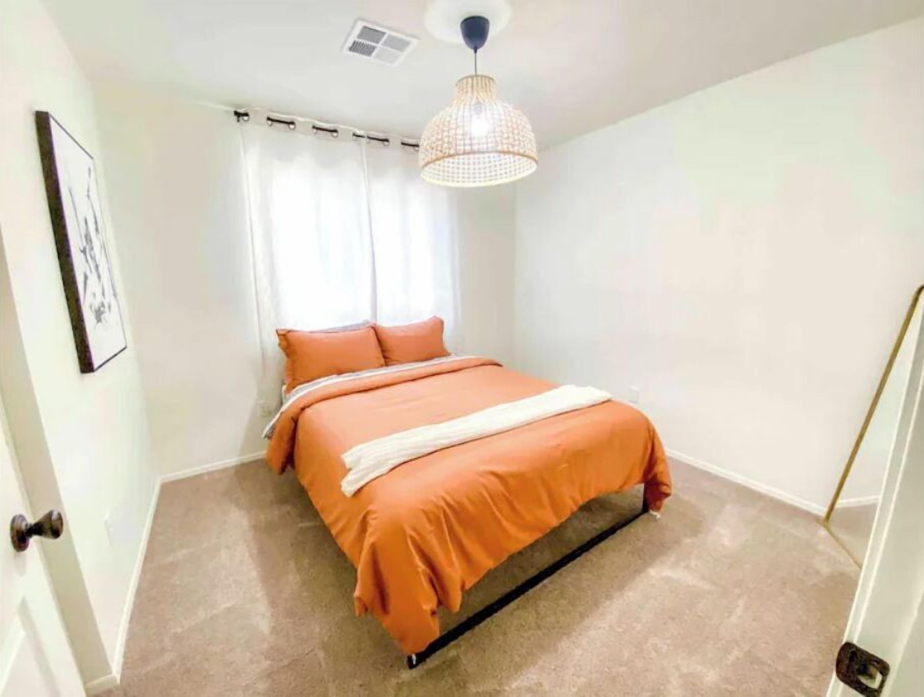 Ein Schlafzimmer mit Bett, weißen Vorhängen, einer Pendelleuchte und einem gerahmten Bild an der Wand.
