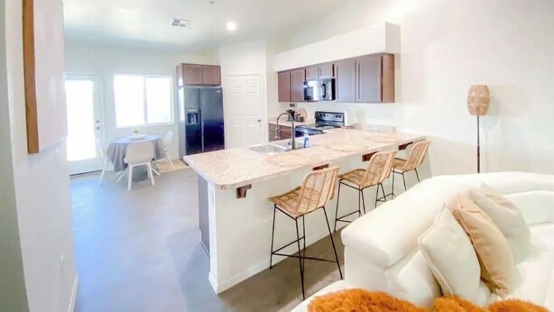 A modern kitchen with a central island, stainless steel appliances, and a dining area with a white table and chairs. - Yuma Boho/Airy 3 bedroom home with free parking (Yuma)