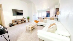 A modern living room with a white sofa, a coffee table, and a flat-screen TV mounted on the wall. - Yuma Boho/Airy 3 bedroom home with free parking (Yuma)