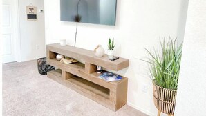 A living room with a wooden entertainment unit, a flat-screen TV, and a potted plant. - Yuma Boho/Airy 3 bedroom home with free parking (Yuma)
