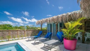 A pool area with lounge chairs, a large potted plant, and a thatched-roof structure. - Un séjour idéal à découvrir  (SAINTE ANNE)