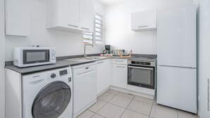 A modern kitchen with white appliances, including a microwave, dishwasher, oven, and refrigerator. - Un séjour idéal à découvrir  (SAINTE ANNE)