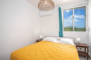 A bedroom with a large bed, a window with curtains, an air conditioning unit, and bedside lamps.