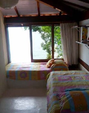 Quarto com duas camas, uma janela com vista para árvores e um ventilador de teto.
