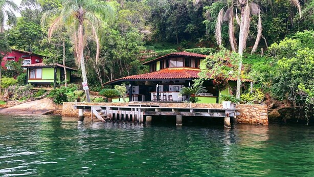 Ein Haus mit rotem Dach, eine Anlegestelle, die in einen See führt, umgeben von üppiger Vegetation und Bäumen.