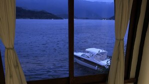 Ein Zimmer mit einem Bett, einem Vorhangfenster und Blick auf ein Gewässer sowie ein Boot.