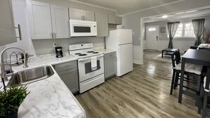 Una cocina moderna con electrodomésticos blancos, encimera de mármol y comedor con mesa y sillas de madera oscura.