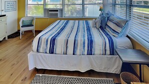 Ein Schlafzimmer mit einem großen Bett, einem Sessel, einem Schreibtisch und einem Fenster mit Jalousien.