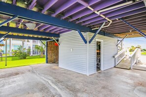 A covered outdoor area with a small building, a concrete floor, and a staircase leading to a deck.