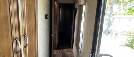 A narrow hallway with wooden doors, a checkered floor, and a fire extinguisher near the door.