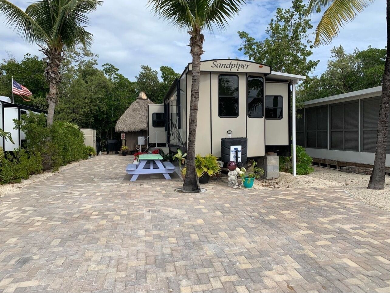 A caravan named 'Sandpiper' with a paved driveway, a picnic table, and palm trees.