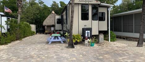 A caravan named 'Sandpiper' with a paved driveway, a picnic table, and palm trees.
