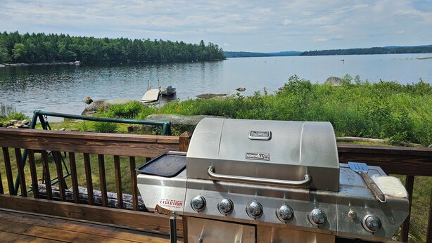 A grill with four burners and a digital display, overlooking a lake with boats and a dock. - Lake House on Great Moose Lake with dock, swimming area, boat landing, and more! (Hartland)