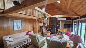 A cozy cabin interior with a loft bed, a sofa, a chair, a table, and a fireplace. - Lake House on Great Moose Lake with dock, swimming area, boat landing, and more! (Hartland)
