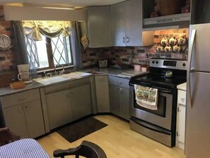 Compact kitchen with oven, microwave, and sink, featuring a window and light-colored cabinets.