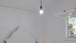 Een slaapkamer met een enkel bed, een nachtkastje, een bedlamp en een raam met uitzicht op bomen.