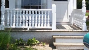 Een witte pergola met een zwarte deur en ramen, omringd door witte balustrades en een trap die erheen leidt.
